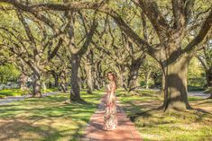 a woman in a long dress is walking down a path lined with trees