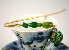 a teacup with some green beads on it and a gold spoon in the cup