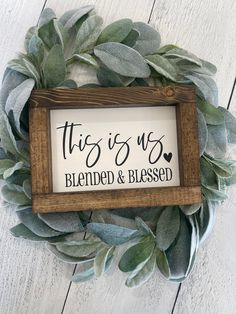 this is us framed sign with greenery around it on a white wooden background that says,'this is us blended & bleased '