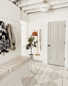 a white room with a bench, coat rack and potted plant