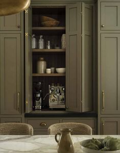 a kitchen with green cabinets and white marble counter tops, an open cabinet door is in the center