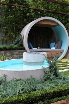 a circular pool in the middle of a garden with plants around it and an outdoor lounge area