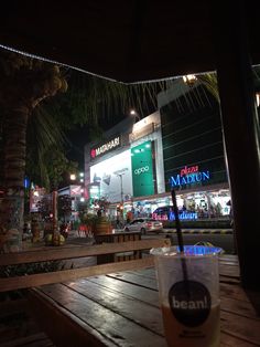 a drink sitting on top of a wooden table in front of a building at night