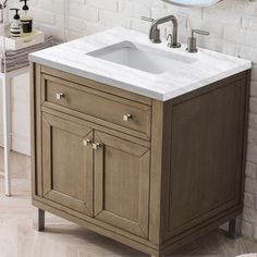 a bathroom sink sitting under a mirror next to a white brick wall and wooden floor