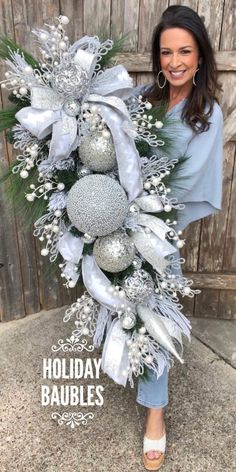 a woman holding a christmas wreath with silver balls and greenery on the front door