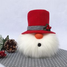 a stuffed snowman wearing a red hat and white fur coat with holly berries on the table