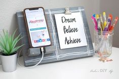 a desk with a cell phone, pen holder and plant on it that says dream believe achieve