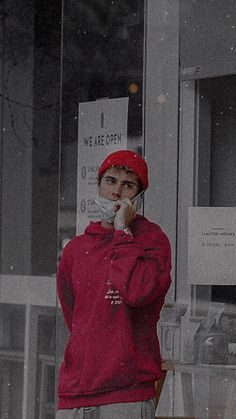 a woman standing in front of a window talking on a cell phone while wearing a red hat