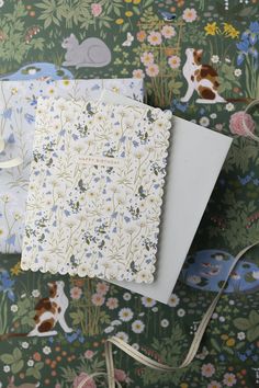 three notebooks are sitting on top of a floral print tablecloth, one is white and the other is blue