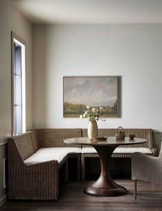 a corner table with two chairs and a vase on it in front of a window