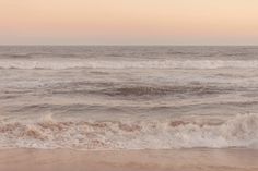 an ocean view with waves crashing on the shore and pink sky in the back ground