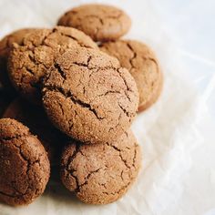 a pile of brown cookies sitting on top of a white table cloth covered in wax paper