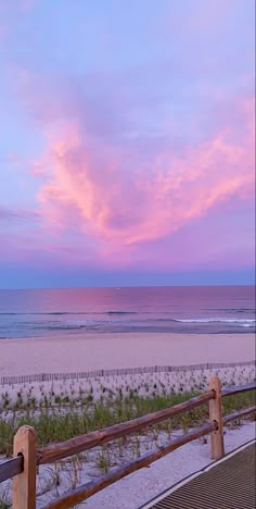 a bench sitting on the side of a sandy beach next to the ocean at sunset