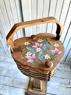 an old wooden basket with flowers painted on the front and sides, sitting on a stand