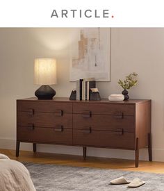 a wooden dresser sitting on top of a carpeted floor next to a lamp and pictures