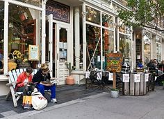 two people sitting on benches in front of a store with lots of windows and plants