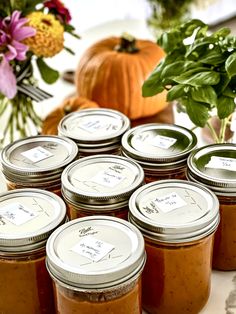 many jars of food are sitting on a table with flowers and pumpkins in the background