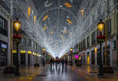 people are walking down the street covered in christmas lights