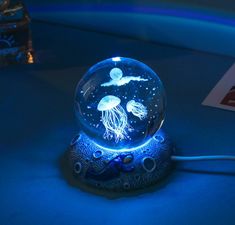 a light up jellyfish in a glass bowl on a blue surface with other items around it