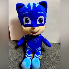 a stuffed animal that is wearing a blue costume and sitting on the floor next to a wall