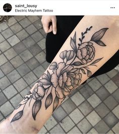 a woman's leg with flowers and leaves tattooed on the side of her arm