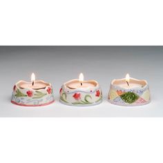 three candles are sitting next to each other on a white surface with flowers and leaves painted on them