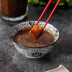 two red chopsticks sticking out of a chocolate drink in a bowl on a table