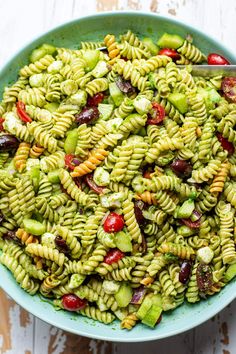 a bowl filled with pasta and vegetables on top of a wooden table next to a fork