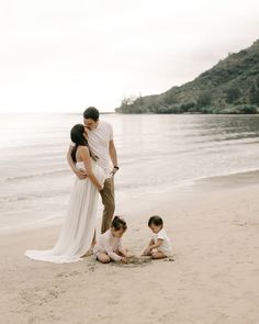 a man and woman standing on top of a sandy beach next to two small children