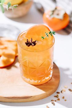 an orange drink sitting on top of a wooden cutting board next to sliced apples and other food