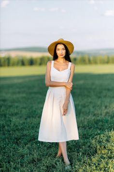 a woman in a white dress and brown hat standing in the middle of a field