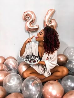 a woman sitting on the ground with balloons and a cake in her hand, surrounded by large numbers