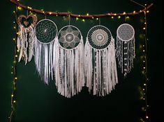 several dream catchers hanging from a string with lights on the wall in the background