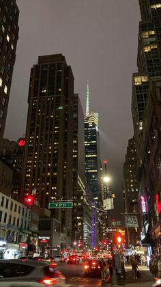 a city street filled with traffic and tall buildings at night, in the distance are skyscrapers