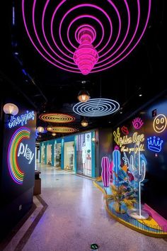 the inside of a brightly lit shopping mall with neon signs on the walls and circular lights hanging from the ceiling