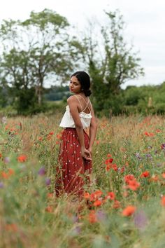 a woman standing in a field full of flowers looking off into the distance with her hands on her hips