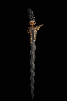 a fancy black and gold hair stick with an elaborate design on the top, is shown against a dark background