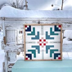 an old wooden bench with a quilt on it's back and some snow in the background