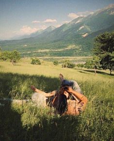 a man laying in the grass with his back to him and mountains in the background