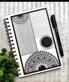 an open notebook with black and white designs on it next to a plant, pen and paper