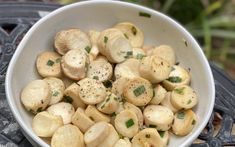 a white bowl filled with sliced mushrooms on top of a black tablecloth next to a potted plant