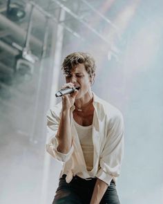 a male in a white shirt and black pants on stage holding a microphone up to his mouth