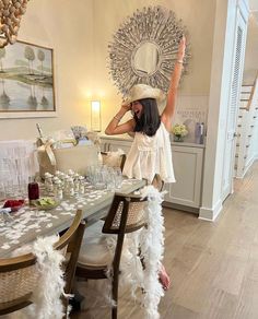 a woman in a white dress and hat standing at a dining room table with feathers on it