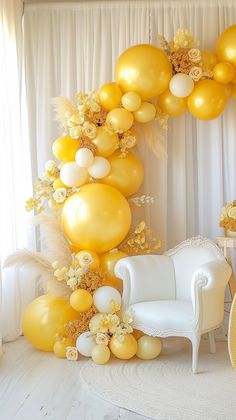 a white chair sitting in front of a yellow and white balloon arch with flowers on it