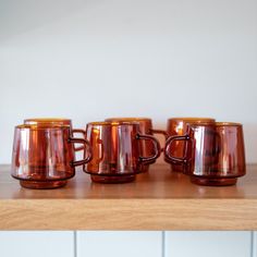 five brown glass mugs sitting on top of a wooden table