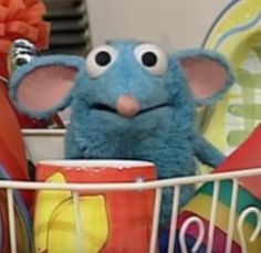 a blue stuffed animal with big eyes in a toy basket filled with toys and plates