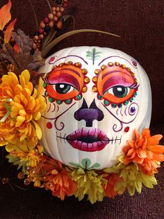 a white pumpkin decorated with orange flowers and a sugar skull on it's head