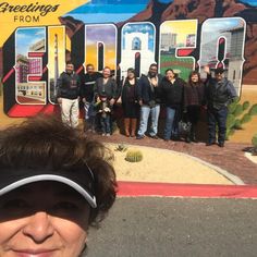 a group of people standing in front of a painted sign that says greetings from arizona