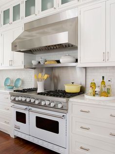 a stove top oven sitting inside of a kitchen next to white cabinets and wooden floors