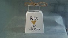 a sign that says ring for a kiss hanging from a rope on a gray background